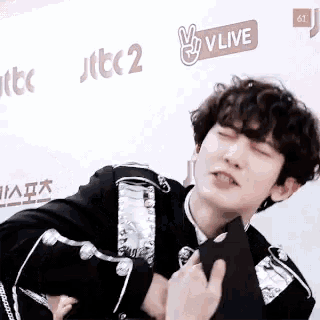 a man with curly hair is standing in front of a sign that says v live