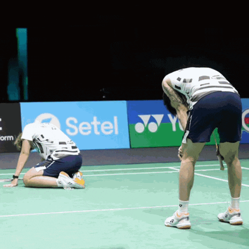 two men are kneeling on a tennis court in front of a setel ad