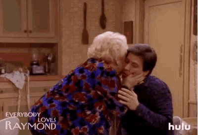 a woman is kissing a man on the cheek in a kitchen from everybody loves raymond .