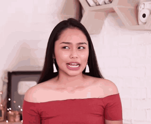 a woman in a red off the shoulder top is making a face