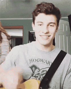 a young man wearing a hogwarts shirt is holding a guitar .