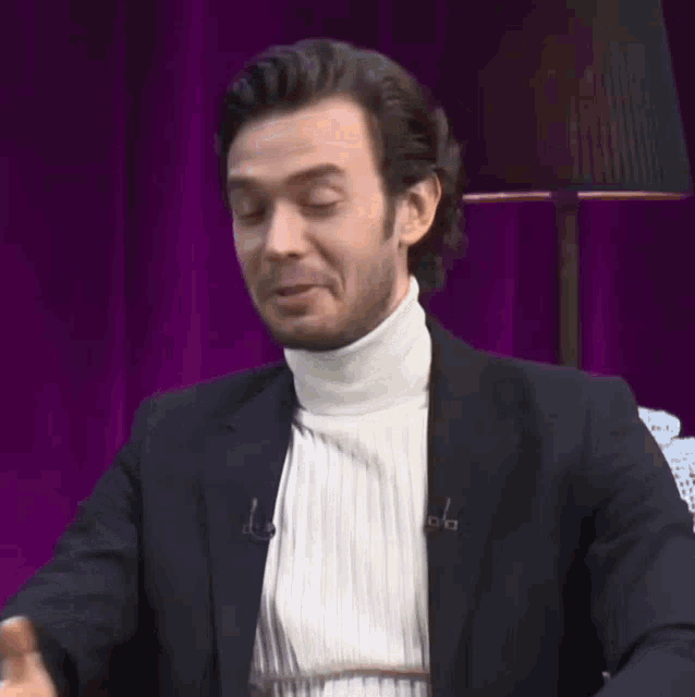 a man wearing a white turtleneck and a black jacket has the letter a on his jacket