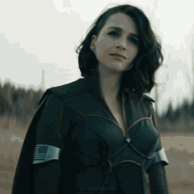 a woman in a black superhero costume is standing in a field looking at the camera .