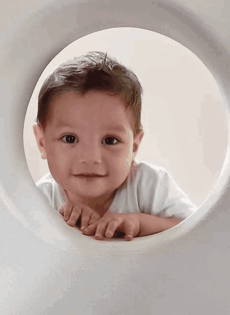 a baby is looking through a hole in a white wall
