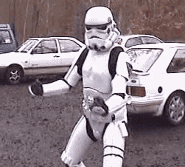 a storm trooper is walking in a parking lot with cars parked behind him .