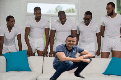 a group of men are squatting around a man on a couch with blue pillows