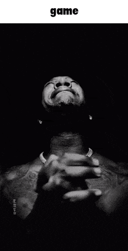 a black and white photo of a man with his hands folded in front of his face and the word game above him