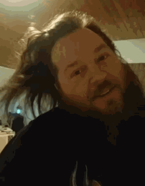 a man with a beard and long hair looks at the camera