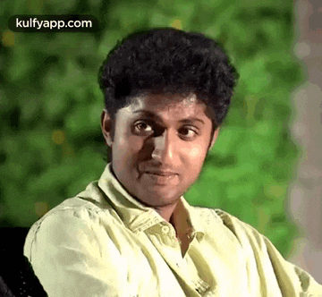 a young man in a yellow shirt is making a funny face while sitting in a chair .