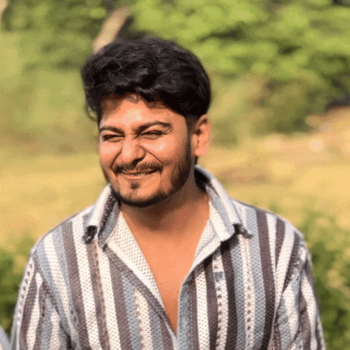 a man with a beard wearing a striped shirt winks at the camera