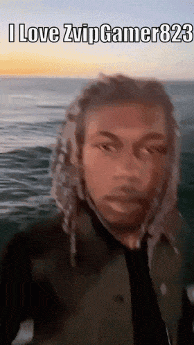 a man with dreadlocks is standing in front of the ocean and says i love zvip gamer823 .
