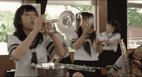 a girl is playing a trumpet in a band while another girl plays a saxophone .