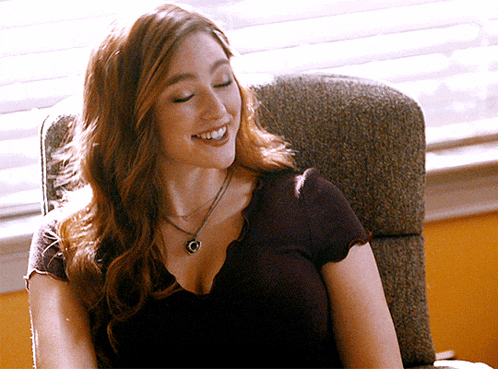 a woman wearing a necklace is smiling while sitting in a chair in front of a window