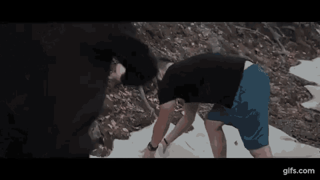a man in a black shirt and blue shorts is kneeling on a snowy hill .