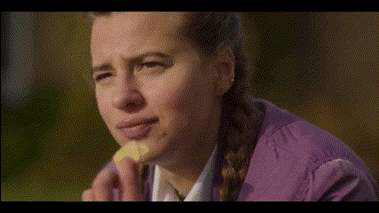 a woman in a purple jacket is eating a piece of bread
