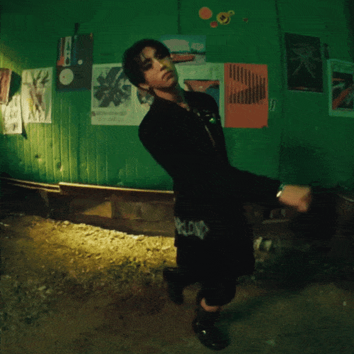 a man in a black jacket is standing in front of a green wall with posters hanging on it