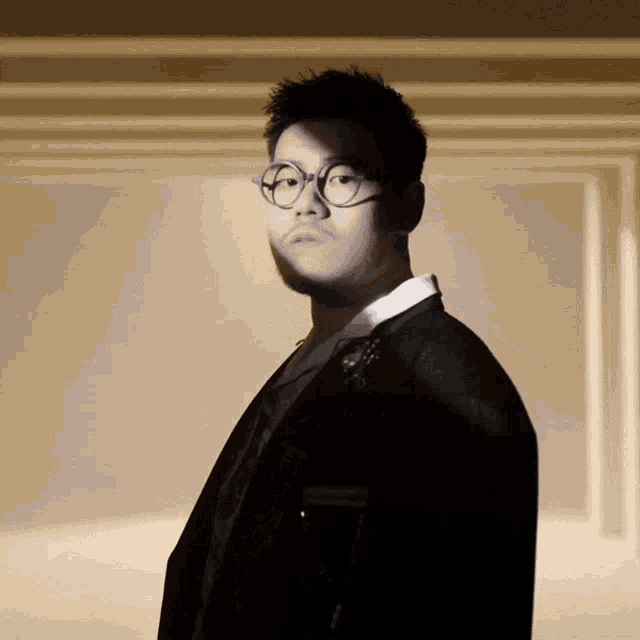 a man wearing glasses and a suit stands in a dark room