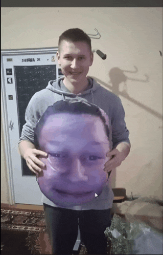 a man holding a pillow with a face on it in front of a door that says silownia
