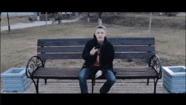 a young man sits on a wooden bench in a park holding a cell phone