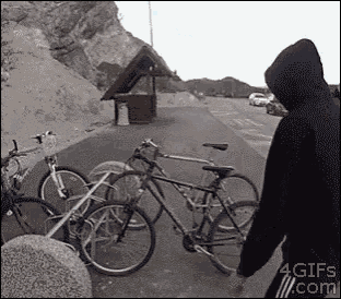 a man in a hoodie is standing next to a row of bicycles on a sidewalk .
