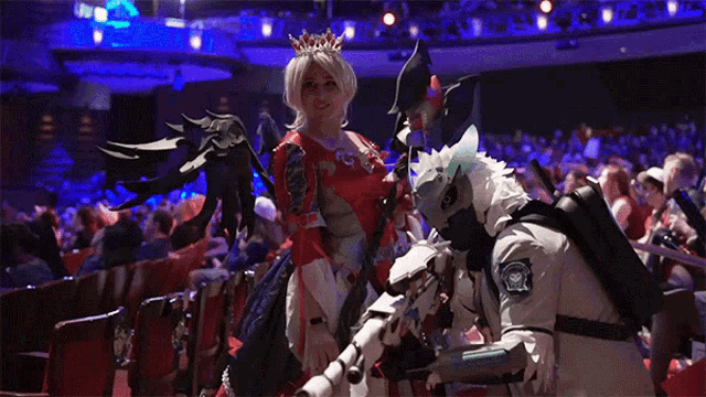 a woman with a crown on her head stands next to a man in a white suit