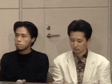 a man in a white jacket sits next to another man in a black sweater