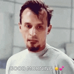 a man with a beard is wearing a gray shirt and saying `` good morning '' .