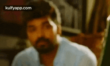 a blurry picture of a man with a beard in a white shirt looking at the camera .