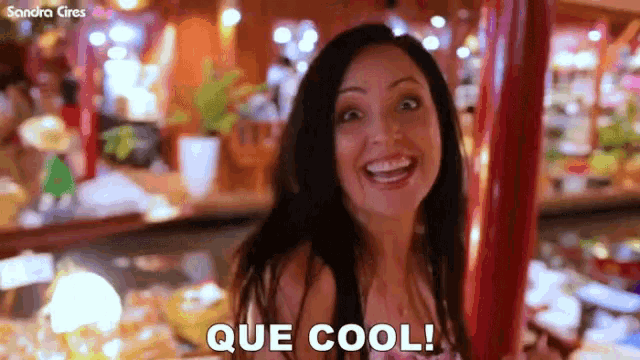 a woman smiles and says que cool in front of a blurry background