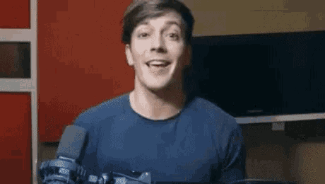 a young man in a blue shirt is holding a camera and smiling .