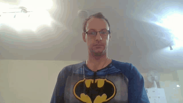 a man wearing glasses and a blue shirt with a batman logo on it