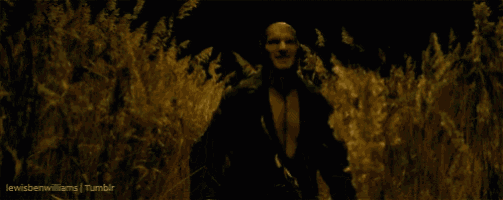 a man is standing in a field of tall grass with a flame coming out of his mouth .