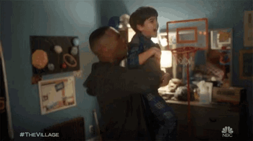a man is holding a little boy in his arms with the hashtag #the village on the bottom