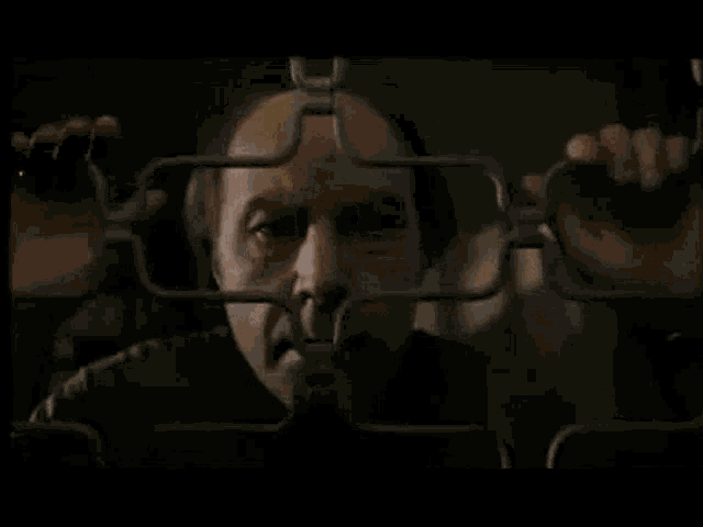 a bald man is behind a metal fence with his hands behind it .