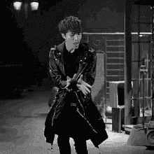 a black and white photo of a man in a leather jacket dancing on a stage .