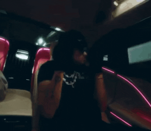 a man in a black shirt and sunglasses is standing in a car with pink lights .