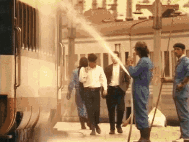 a group of men are walking towards a train while a man sprays water on them