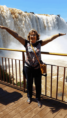 a woman with her arms outstretched stands in front of a waterfall