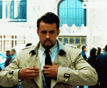 a man in a trench coat and tie is adjusting his tie