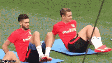 two soccer players are doing sit ups on a mat on the field .