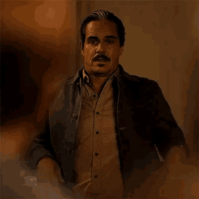 a man in a black jacket is standing in front of a wall .