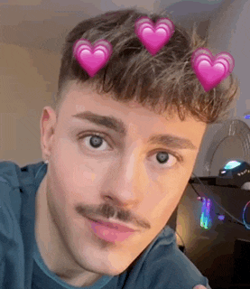 a young man with a mustache and hearts in his hair is looking at the camera .
