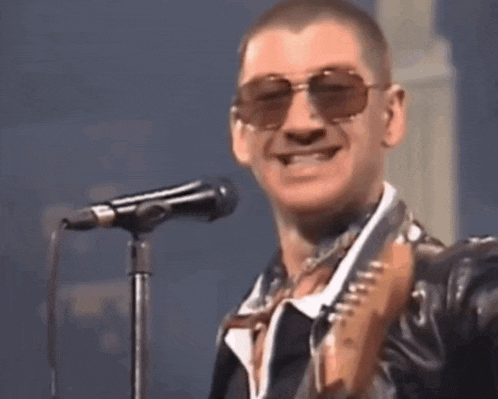 a man wearing sunglasses is singing into a microphone and playing a guitar .