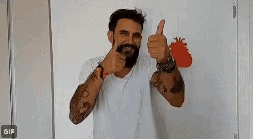 a man with a beard is giving two thumbs up in front of a heart on a wall .