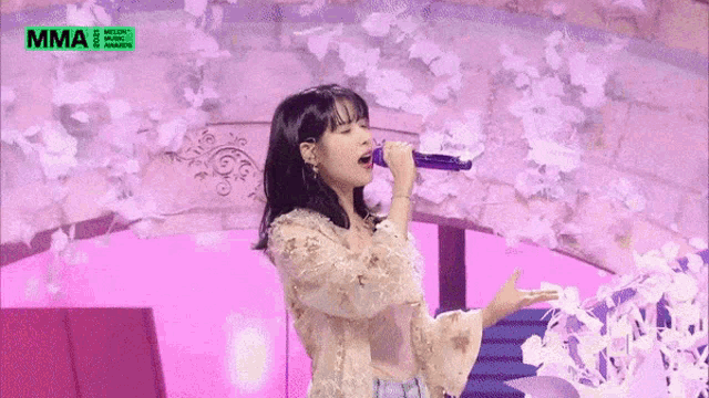 a woman singing into a microphone in front of a sign that says mma on it