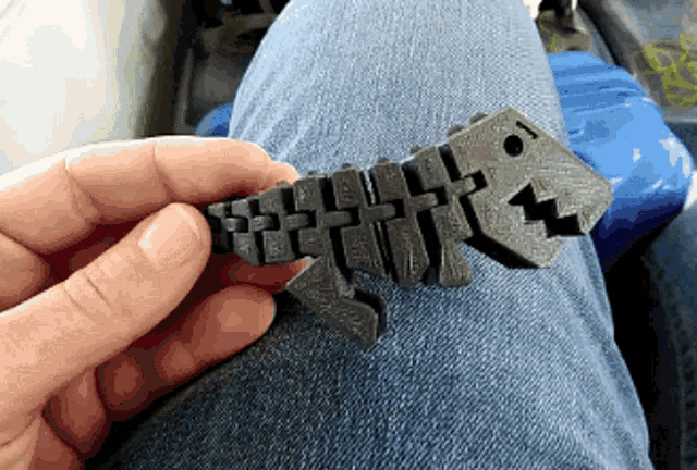 a person is holding a 3d printed dinosaur toy