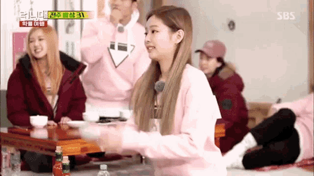 a woman in a pink sweater is sitting at a table in a room with other people .