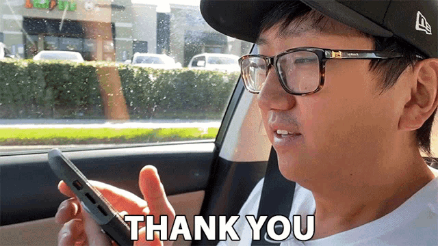 a man wearing glasses and a hat says thank you while looking at his cell phone