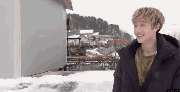 a young man is standing in the snow in front of a building and smiling .