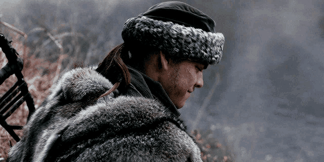 a man wearing a fur coat and a hat is standing in a field .